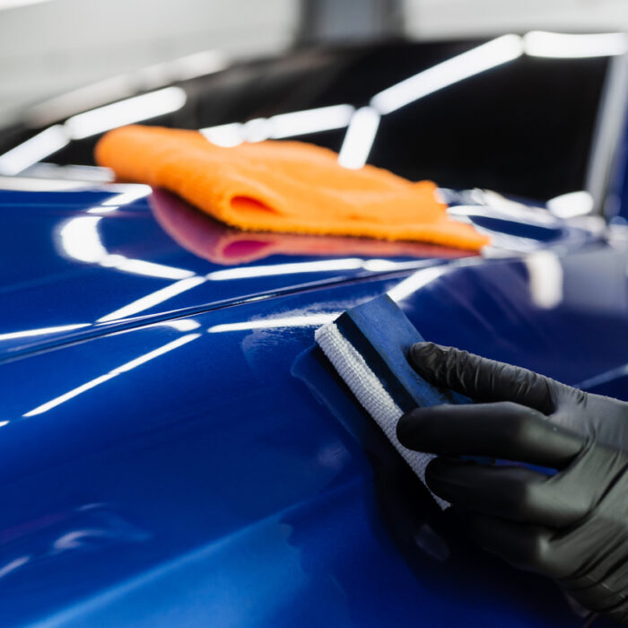 Process of applying ceramic protective coat on body car using sponge in detailing auto service. Car service worker apply ceramic coating to protect the car body from scratches.