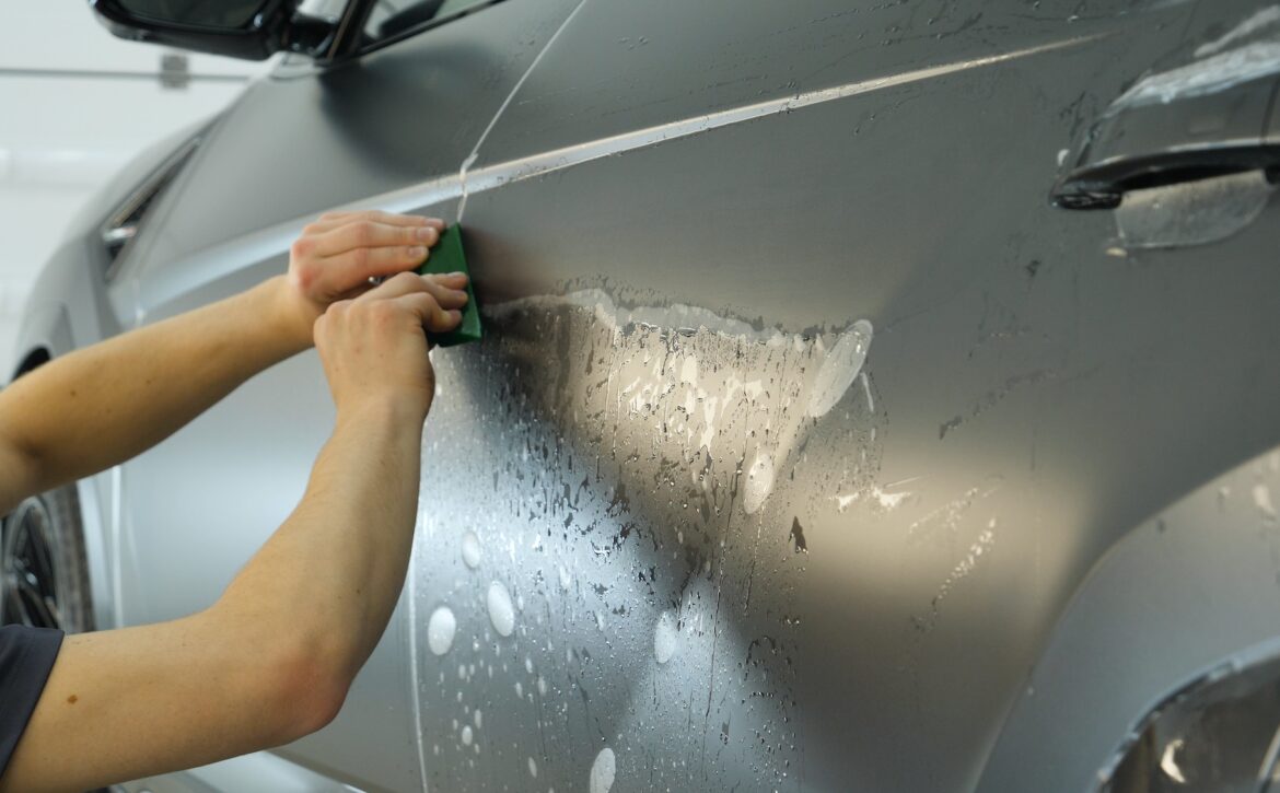 Close up of paint protection film installation on modern luxury car. PPF is polyurethane film that wrap car paint to protect paint surface from stone chips, bug splatter, and abrasion.